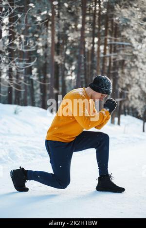Sportlicher Mann, der während seines Wintertrainings im Schneepark Ausfallschritte macht Stockfoto
