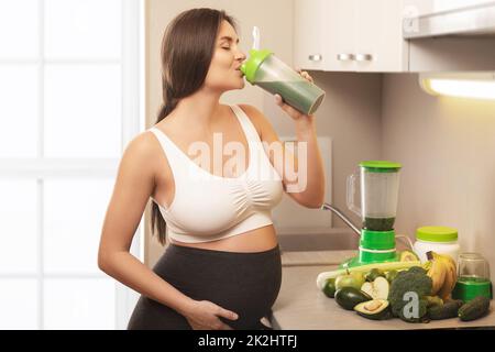 Glückliche, schwanger Frau trinkt grünen Protein-Cocktail Stockfoto