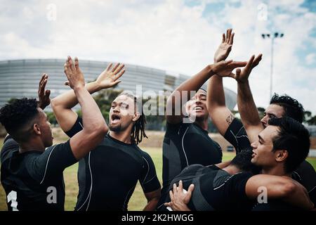 Sie sind so großartig zu gewinnen. Eine kurze Aufnahme eines Teams von Rugby-Spielern, die feiern, während sie tagsüber auf dem Spielfeld stehen. Stockfoto