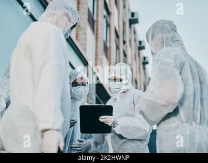 Teamarbeit macht Infektionskontrolle zum Erfolg. Aufnahme einer Gruppe von Mitarbeitern im Gesundheitswesen, die in Gefahrgutanzügen arbeiten und während eines Ausbruchs in der Stadt zusammenarbeiten. Stockfoto