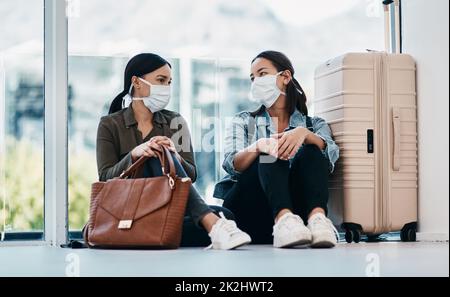 Es dauerte eine Distanz, um uns zu verbinden. Aufnahme von zwei jungen Frauen, die Masken tragen, während sie gemeinsam auf einem Flughafen warten. Stockfoto