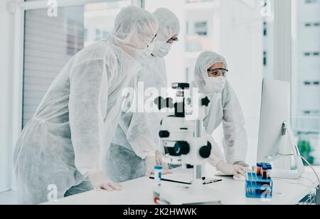 Die Heilung ist so nahe. Aufnahme einer Gruppe von Wissenschaftlern in Hazmat-Anzügen, die medizinische Forschung in einem Labor durchführen. Stockfoto