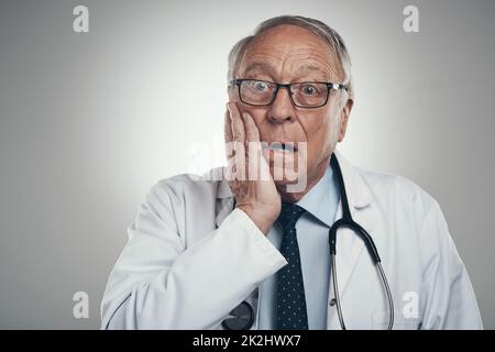 Ich habe das nicht kommen sehen. Aufnahme eines älteren männlichen Arztes in einem Studio vor grauem Hintergrund. Stockfoto