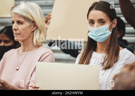 Du musst für die Freiheit kämpfen. Ein Porträt einer attraktiven jungen Frau, die eine Maske trägt, während sie an einer politischen Kundgebung teilnimmt. Stockfoto