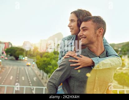 Junge urbane Liebe. Aufnahme eines glücklichen jungen Paares, das eine Huckepack-Fahrt in der Stadt genießt. Stockfoto