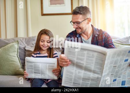 Sehen Sie alles interessante. Aufnahme eines Vaters und einer Tochter beim Lesen der Zeitung. Stockfoto