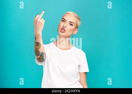 Bleiben Sie auf der Spur. Studioaufnahme einer jungen Frau, die ihren Mittelfinger vor türkisfarbenem Hintergrund zeigt. Stockfoto