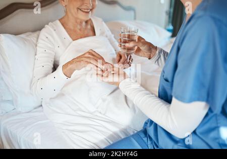 Zuverlässige Behandlung liegt in ihren Händen. Aufnahme einer Krankenschwester, die einer älteren Frau mit einem Glas Wasser im Bett Medikamente gab. Stockfoto