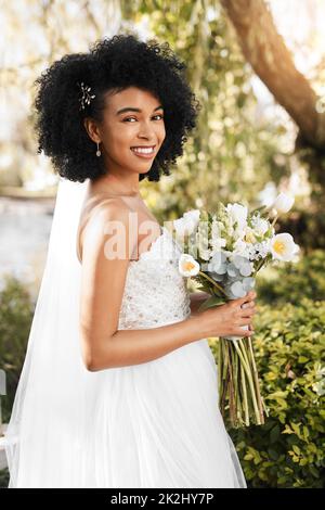 Ich bin bereit zu sagen, dass ich es tue. Porträt einer glücklichen und schönen jungen Braut mit einem Blumenstrauß, während sie an ihrem Hochzeitstag im Freien posiert. Stockfoto