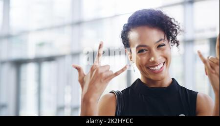 Das Geschäft boomt. Ausgeschnittene Aufnahme einer jungen Geschäftsfrau, die ein Rock'n Roll-Schild zeigt, während sie durch ein modernes Büro geht. Stockfoto