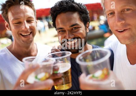 Bier mit den Jungs. Drei junge Männer toasten ihr Bier auf einem Musikfestival. Stockfoto