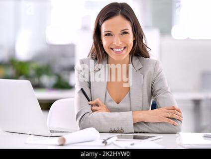 Sie hat es geschafft. Aufnahme einer attraktiven Geschäftsfrau, die in einem Büro an ihrem Schreibtisch sitzt. Stockfoto