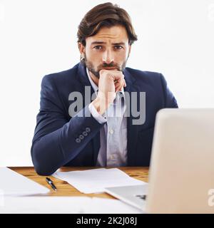 Lassen Sie mich darüber nachdenken. Aufnahme eines selbstbewussten jungen Geschäftsmannes, der an seinem Laptop arbeitet und die Kamera anschaut. Stockfoto