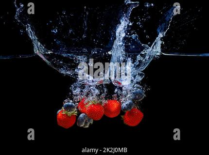 Mischung aus frischen Erdbeeren und Heidelbeeren in Wasser mit Spritzern isoliert auf schwarzem Hintergrund gefallen. Stockfoto