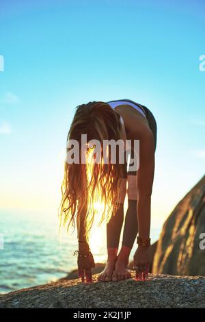 Yoga lässt dich lebendig werden. Aufnahme einer athletischen jungen Frau, die am Strand Yoga praktiziert. Stockfoto