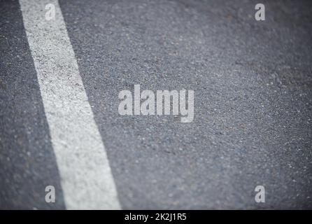 Auf die Straße. Nahaufnahme einer weißen Trennlinie auf einer asphaltierten Straße. Stockfoto