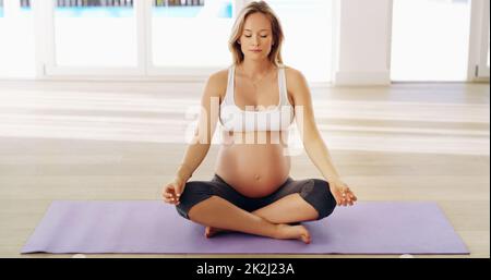 Innere Ruhe finden. Ganzkörperaufnahme einer attraktiven jungen Schwangeren, die auf einer Yogamatte meditiert. Stockfoto