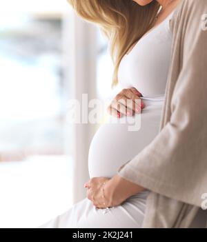 Ihr Baby ist in liebevollen Händen. Kurzer Schuss einer unkenntlich werdenden Schwangeren, die zu Hause sitzt. Stockfoto