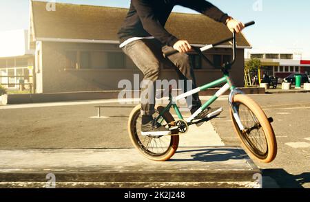 Auf die Straße. Zugeschnittenes Bild eines nicht erkennbaren männlichen BMX-Bikers, der draußen Tricks macht. Stockfoto