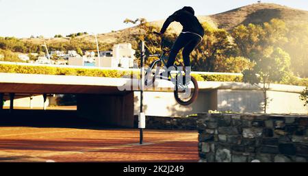 Gehen Sie groß oder Geh nach Hause. Ganzkörperaufnahme eines jungen BMX-Reiters, der Tricks in der Stadt macht. Stockfoto