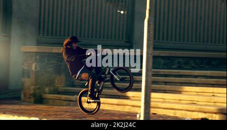 Ein Wheelie knallen. Ganzkörperaufnahme eines jungen BMX-Reiters, der Tricks in der Stadt macht. Stockfoto