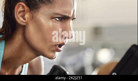 Diszipliniert und entschlossen. Eine kurze Aufnahme einer entschlossen aussehenden jungen Frau, die im Fitnessstudio an einem Crosstrainer arbeitet. Stockfoto