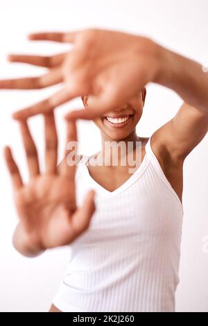 Das Lächeln ist alles, was wir sehen müssen. Studioaufnahme einer unkenntlichen Frau, die sich hinter ihren Händen versteckt. Stockfoto