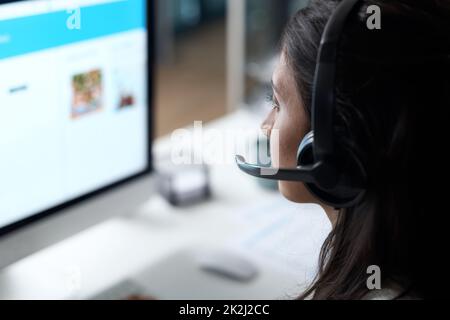 Umfassende Fähigkeiten bei der Bereitstellung von qualitativ hochwertigem Kundensupport. Aufnahme einer jungen Frau, die in einem modernen Büro ein Headset und einen Computer benutzt. Stockfoto