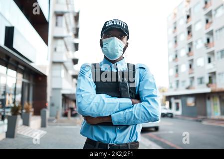 Ich setze den Profi in Protect. Porträt eines selbstbewussten maskierten jungen Wachbeamten, der draußen Wache steht. Stockfoto