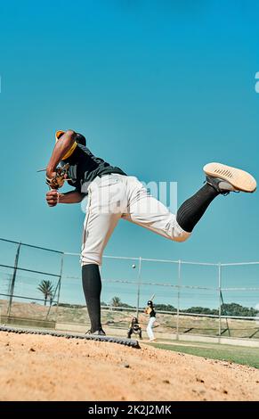 Hes gibt ihm sein alles. Aufnahme eines jungen Baseballspielers, der den Ball während eines Spiels im Freien anspielt. Stockfoto