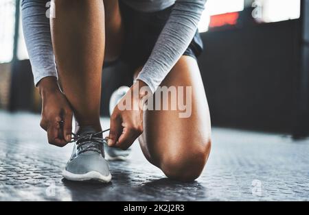 Schnalle dich an und los geht es. Eine kurze Aufnahme einer Frau, die ihre Schnürsenkel in einem Fitnessstudio bindet. Stockfoto