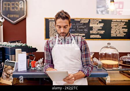 Hier finden Sie die neuesten Kaffeetrends. Aufnahme eines jungen Barista mit einem digitalen Tablet in einem Café. Stockfoto