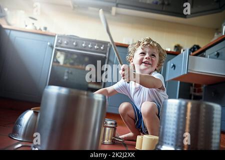 Man könnte es Lärm nennen, aber Kinder nennen es Spaß. Aufnahme eines entzückenden kleinen Jungen, der in der Küche Trommeln auf Töpfen spielt. Stockfoto