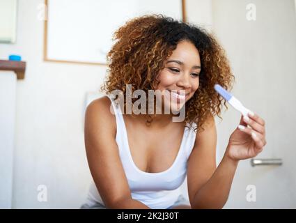 Ich kann es kaum erwarten, die guten Nachrichten zu teilen. Aufnahme einer jungen Frau, die sich die Ergebnisse ihres Schwangerschaftstests ansieht. Stockfoto