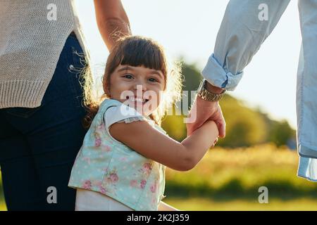 Und los geht's in den Park. Porträt eines entzückenden und glücklichen kleinen Mädchens, das ihre Mutter und ihren Vater im Park in der Hand hält. Stockfoto