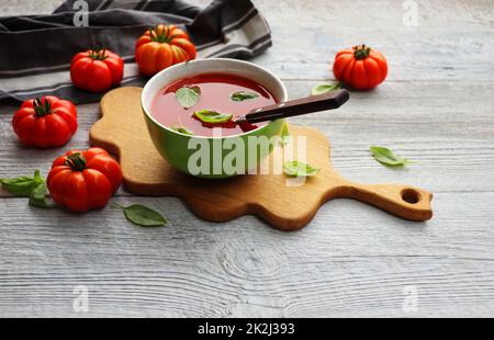 Eine Schüssel mit frischem Gazpacho, kalte Tomatensuppe mit Basilikumblättern auf grauem Hintergrund Stockfoto