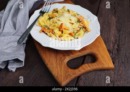 Pasta mit Bio-Pfifferlingen. Portion Pasta mit gebratenen Pfifferlingen in einer cremigen Knoblauchsauce mit Käse aus nächster Nähe auf einem Teller auf dem Tisch Stockfoto