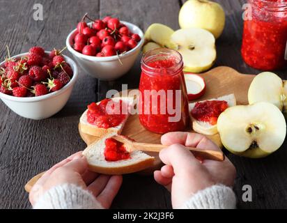 Glas mit verschiedenen Arten von Beeren und Früchten auf Holztisch. Apfel, Himbeere, Weißdornmarmelade Stockfoto