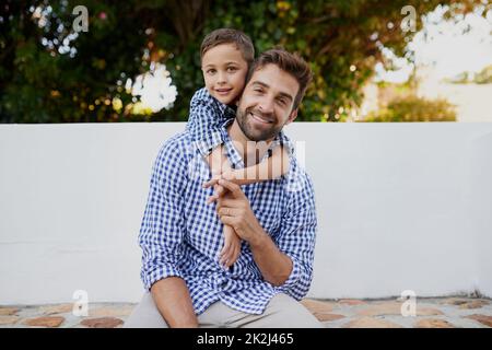 Hes ein kleines Mini Me. Beschnittenes Porträt eines hübschen jungen Mannes und seines Sohnes, die draußen sitzen. Stockfoto