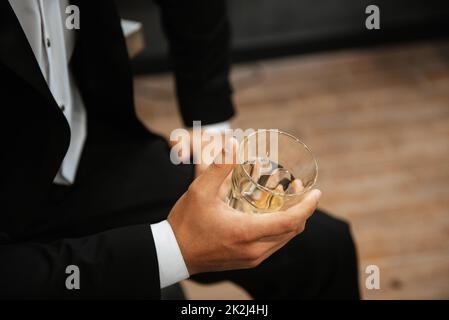 Ein Glas Whiskey in der Hand eines Mannes in einem schwarzen Anzug Stockfoto