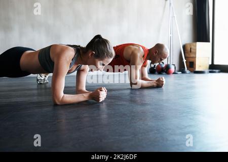 Drücke dich in die Fitness. Aufnahme eines Mannes und einer Frau, die im Fitnessstudio Plank-Übungen machen. Stockfoto