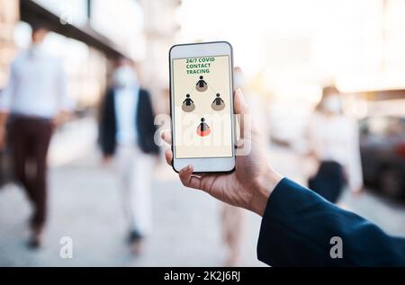 Die Früherkennung macht den Unterschied. Aufnahme einer nicht erkennbaren Frau mit einer Covid-19 Tracking-App auf ihrem Smartphone in der Stadt. Stockfoto