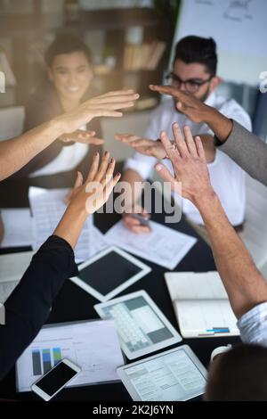 Erfolg hat für dieses Team oberste Priorität. Aufnahme einer Gruppe von Mitarbeitern mit ihren Händen in einem Geheule, während sie zusammen um einen Tisch in einem Büro sitzen. Stockfoto