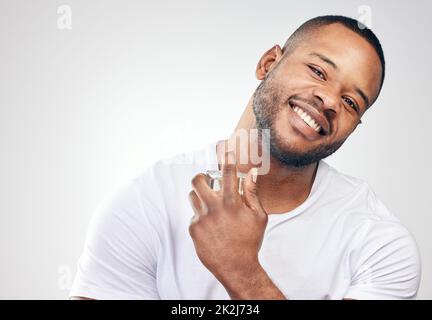 Ein Gentleman, der sauber ist und gut riecht, wird immer attraktiv sein. Studio-Porträt eines gutaussehenden jungen Mannes, der sich vor weißem Hintergrund mit Parfüm besprüht. Stockfoto