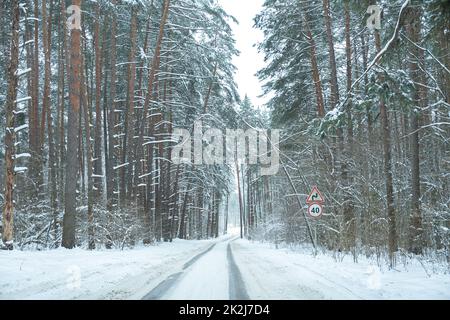 Winterlicher Schneefall auf der Straße. Eine leere Landstraße ohne Autos, bedeckt mit Schneeverwehungen. Reisen Sie bei schlechtem Wetter. Winter wolkige Landschaft mit einer Landstraße. T Stockfoto