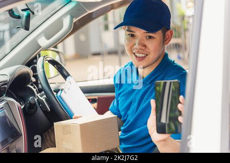 Ein Transporteur, der die Lieferung online bereitstellt, lädt die Kartons im Auto aus und überprüft den Standort über ein mobiles Smartphone Stockfoto