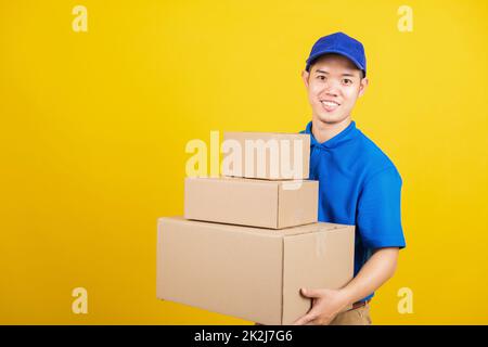 Portrait aufgeregt attraktive Lieferung glücklich Mann logistischen stehend er lächeln in blauen T-Shirt und Mütze Uniform halten Paketkasten Blick auf die Kamera, Studioaufnahme isoliert auf gelbem Hintergrund Stockfoto