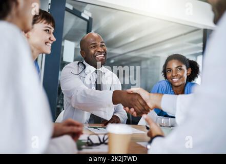 Bringen Sie einen neuen Arzt an Bord. Aufnahme von Ärzten, die sich während eines Treffens in einem Krankenhaus die Hände schüttelten. Stockfoto