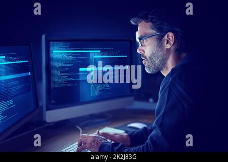 Eingebettet in die Metadaten. Aufnahme eines fokussierten Computerhackers, der einen Computer im Dunkeln benutzt. Stockfoto