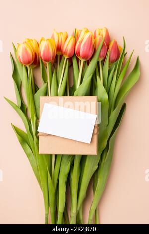 Grußkarten-Mockup oder Dankeskarte-Vorlage. Bouquet von Tulpen und einer Geschenkbox auf beigem Hintergrund. Stockfoto
